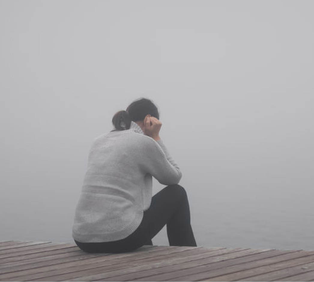 Eine Frau sitzt auf einem Steg im Nebel an einem See – Symbol für Krisen und Orientierungslosigkeit